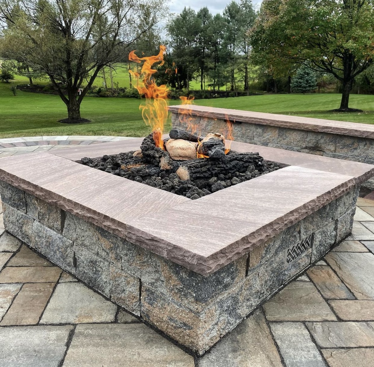 Lit stone fire pit on a paver patio with a stacked-stone seat wall